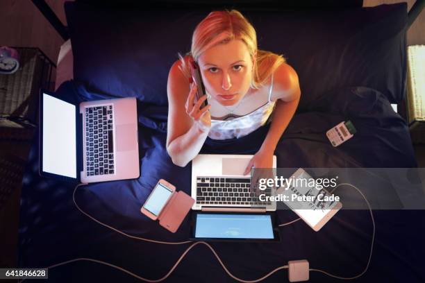 woman sat in bed at night, surrounded by technologhy, working - crouler sous le travail photos et images de collection