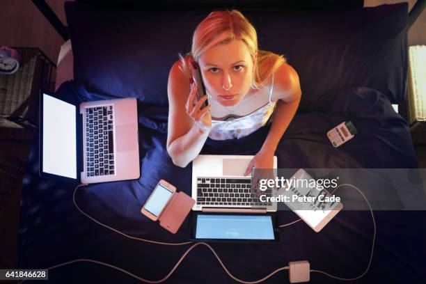woman sat in bed at night, surrounded by technologhy, working - overwerkt stockfoto's en -beelden