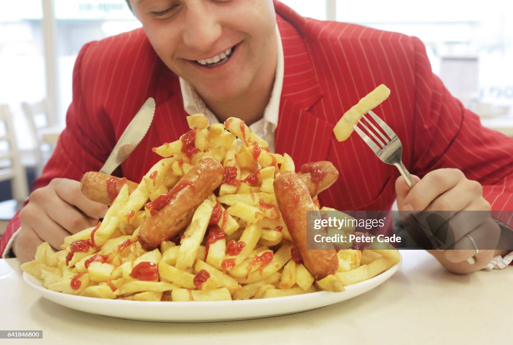 Man in red suit eating large plate of sausages and chips