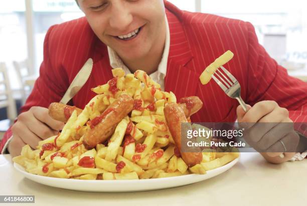 man in red suit eating large plate of sausages and chips - portion imagens e fotografias de stock