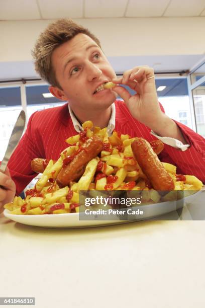 man in red suit eating large plate of sausages and chips - frites stock pictures, royalty-free photos & images