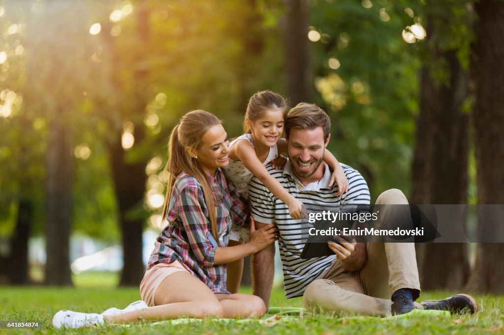 Happy family using digital tablet in the park.