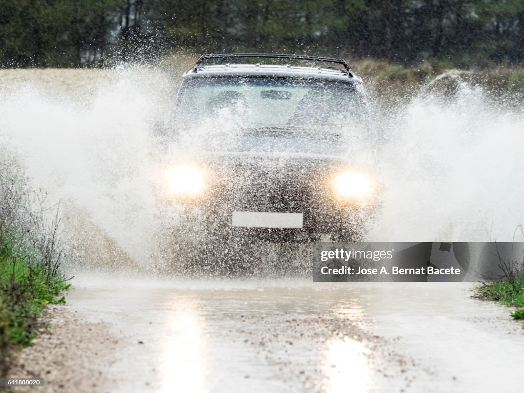 4x4 vehicle on muddy road splashing past a large puddle of rainwater, Spain.