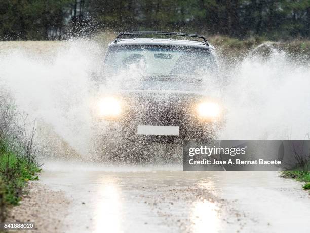 4x4 vehicle on muddy road splashing past a large puddle of rainwater, spain. - torrential rain stockfoto's en -beelden