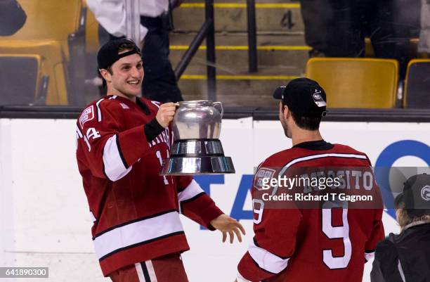 Alexander Kerfoot of the Harvard Crimson hands-off the Beanpot trophy to teammte Luke Esposito after beating the Boston University Terriers during...