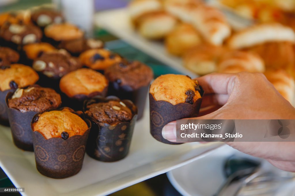 Young men taking raisin chocolate muffin at breakfast