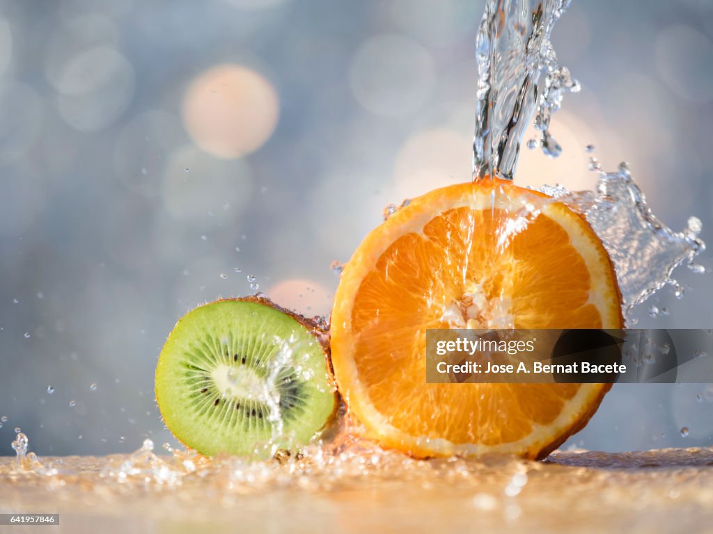 Half of an orange and a kiwi washed with a water jet in the kitchen, illuminated by the light of the Sun