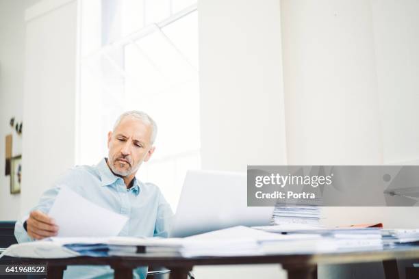 geschäftsmann lesen von dokumenten am schreibtisch in büro - mature reading computer stock-fotos und bilder