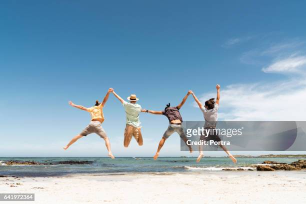 achteraanzicht van vrienden springen op strand - group sea stockfoto's en -beelden