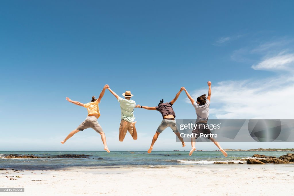 Rear view of friends jumping at beach