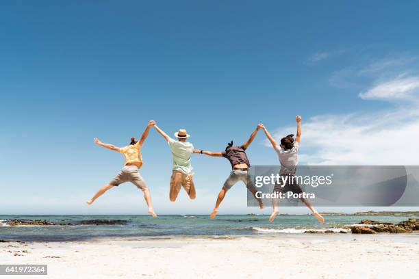 rear view of friends jumping at beach - só homens jovens imagens e fotografias de stock