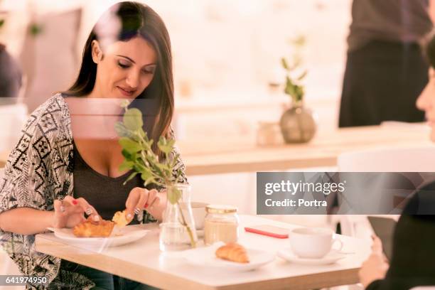 smiling woman breaking croissant at table in cafe - breaking croissant stock pictures, royalty-free photos & images