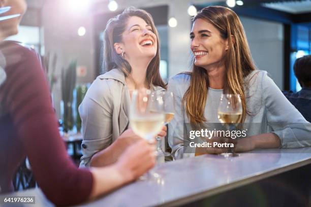 friends laughing while enjoying drinks in bar - brown hair drink wine stock pictures, royalty-free photos & images