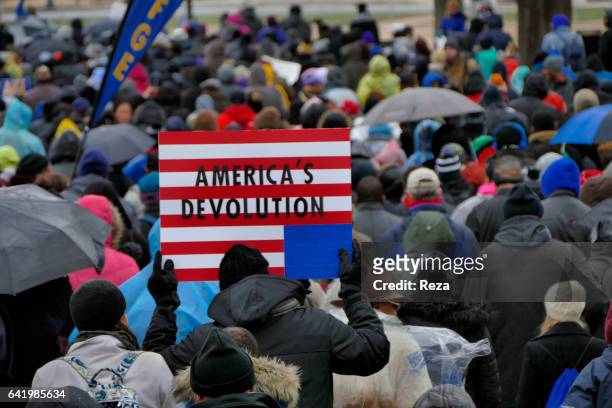 On Martin Luther King Day, hundreds gather around for a commemorative walk. "nA man holds a placard saying "America's Devolution". Devolution...