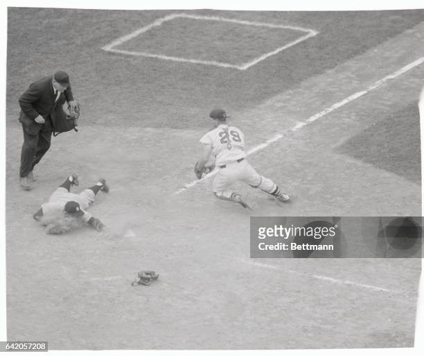 Yogi Berra of the New York Yankees slides safely across the plate, head-first, after tagging up at third base as Yanks' Cletis Boyer hit foul fly to...
