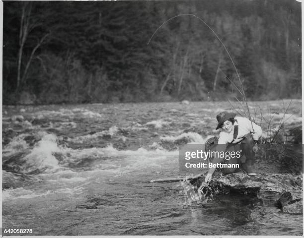 After hooking and playing her game quarry, Alice Williams of Seattle, Washington, nets a big trout in one of the swift-flowing streams of Western...