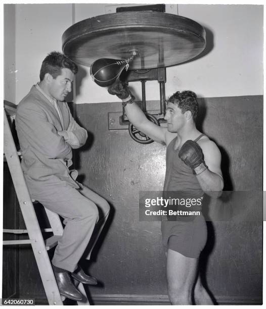 New York, NY- Middleweight Rocky Graziano visits heavyweight Rocky Marciano, as the latter works out on the light bag, for his fight with Roland...