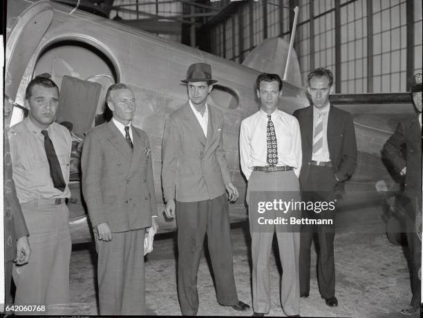 Howard Hughes, millionaire aviator and film producer, is pictured above with four members of his crew after he landed his twin-motored Lockheed 14...