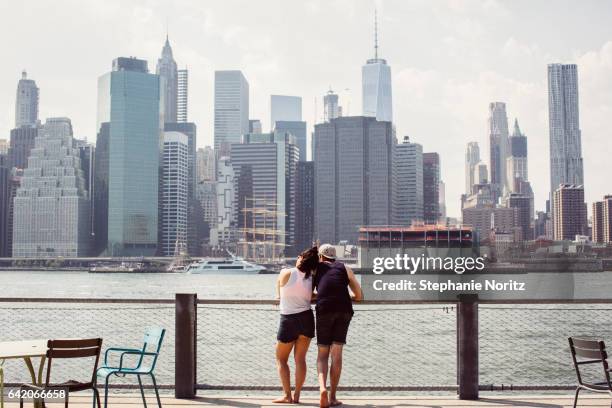 young couple leaning on one another looking at manhattan skyline - brooklyn skyline foto e immagini stock