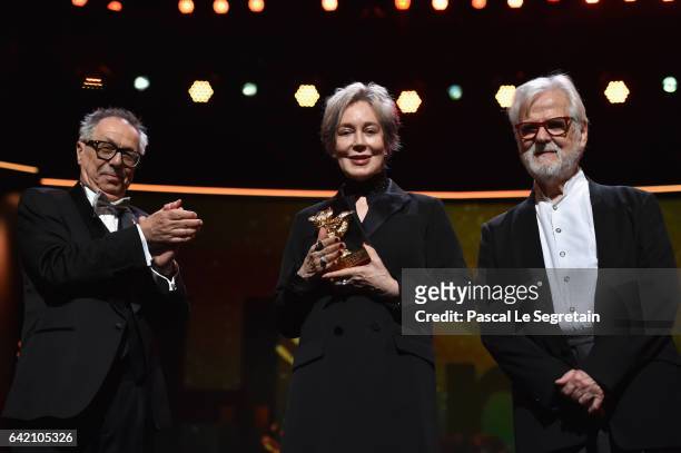 Festival director Dieter Kosslick applauds costume designer Milena Canonero on stage as she receives her honorary Golden Bear next to producer Jan...
