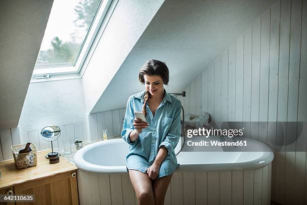 young woman in bathroom using smartphone - mid adult women stock pictures, royalty-free photos & images