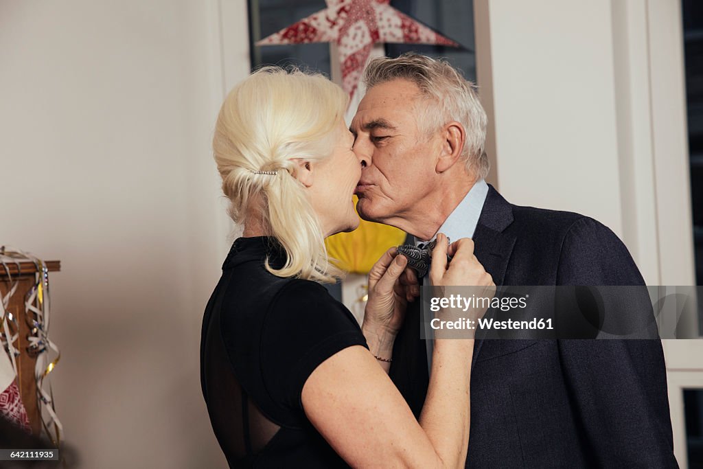 Senior couple kissing while fastening bow tie for New Year's Eve party