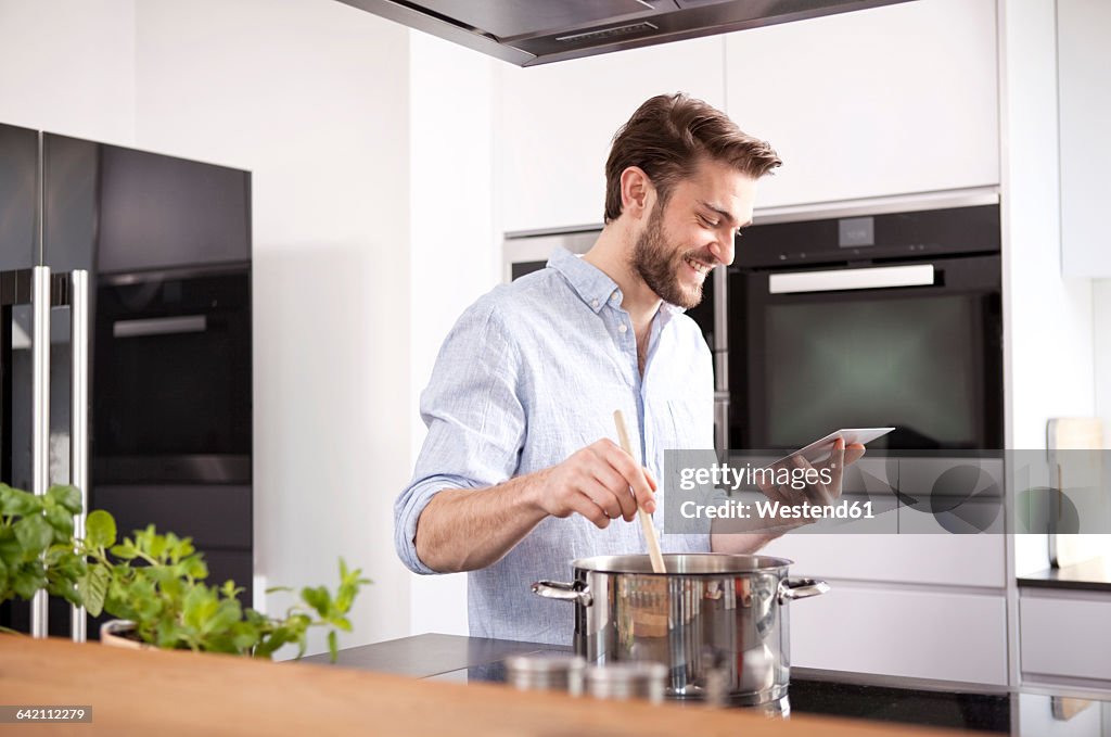 Young man looking at with mini tablet while cooking