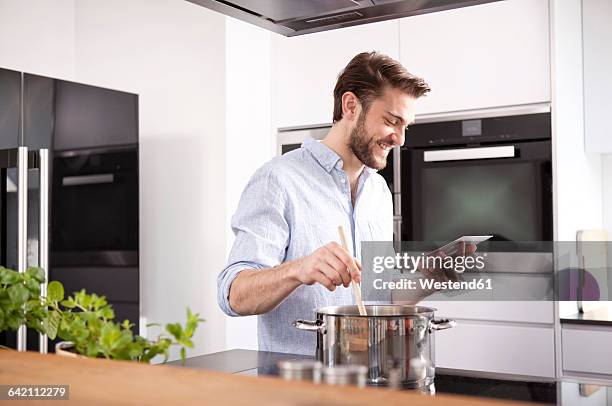 young man looking at with mini tablet while cooking - stirring stock pictures, royalty-free photos & images