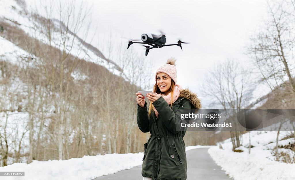 Spain, Asturias, young woman navigating a drone in the snowy mountains