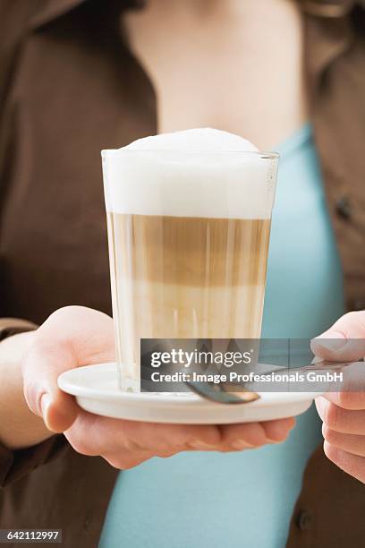 woman holding a glass of latte macchiato - milchschaum stock-fotos und bilder