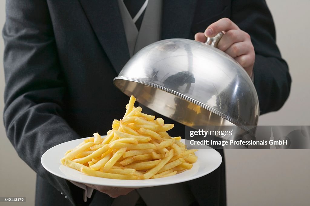 Butler lifting serving dome from plate of chips