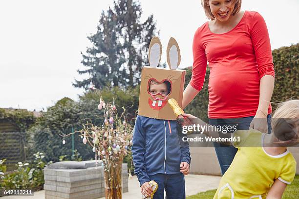 pregnant mother with boy wearing bunny mask and happy girl in garden - chocolate bunny stock-fotos und bilder