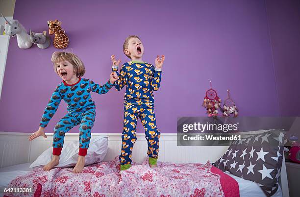 brother and sister wearing pajamas romping around in children's room - kid jumping stock-fotos und bilder