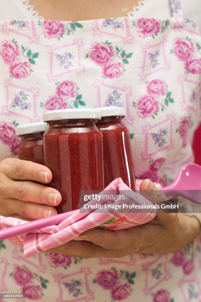 Woman holding jars of jam, tea towel and kitchen spoon