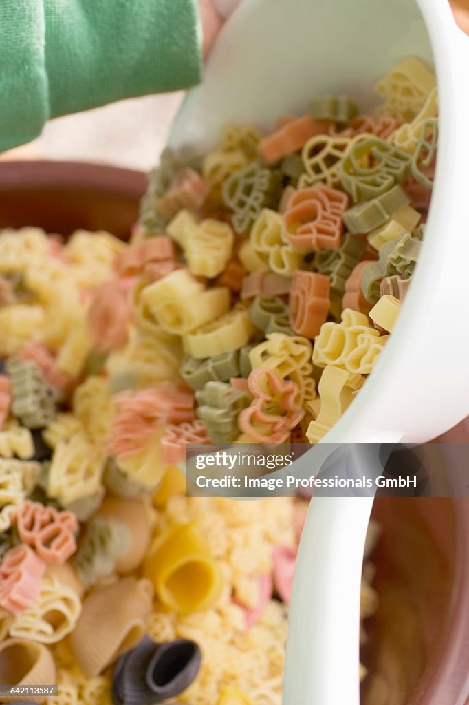 Child tipping coloured pasta out of strainer into bowl