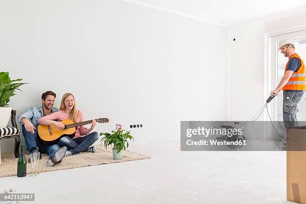 happy couple playing guitar and singing at their new home while - teppich unfertig stock-fotos und bilder