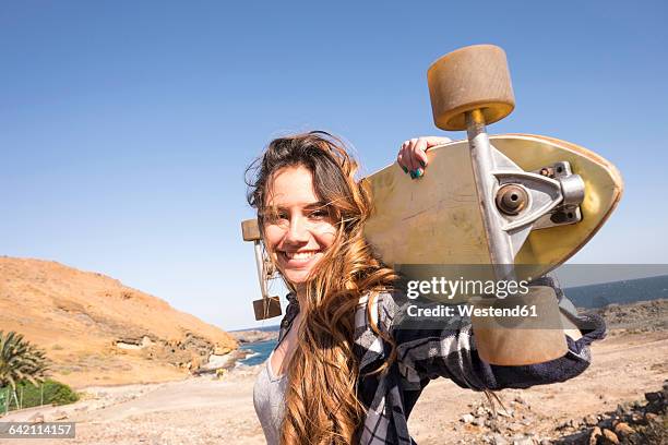 spain, portrait of smiling teenage girl with longboard on shoulders - tenerife stock-fotos und bilder