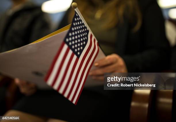 Newly sworn in US citizen holds a US flag while listening to a speech from a US government employee at a naturalization ceremony for new US citizens...