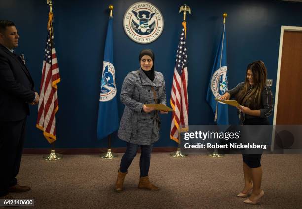 Newly sworn in US citizen, center, receives her Certificate of Naturalization from a US government employee, right, during a naturalization ceremony...