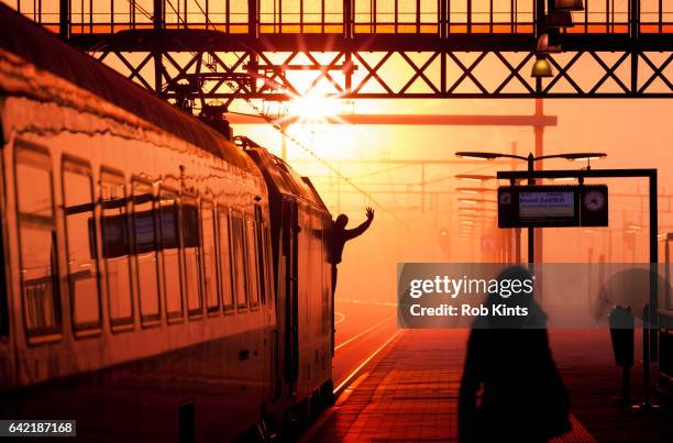 train driver in locomotive waving as the train departs from station at sunset - treinstation - fotografias e filmes do acervo