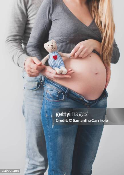 pregnant woman and her husband holding a little peluche bear with heart symbol. white background. couple. - peluche ストックフォトと画像
