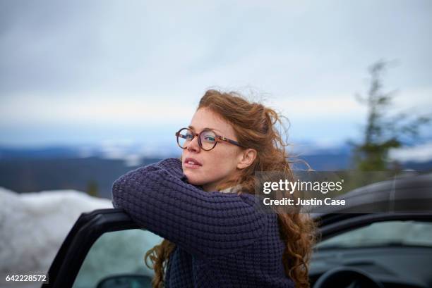 woman leaning on her car door overlooking landscape while having a break from driving - brillen stock-fotos und bilder