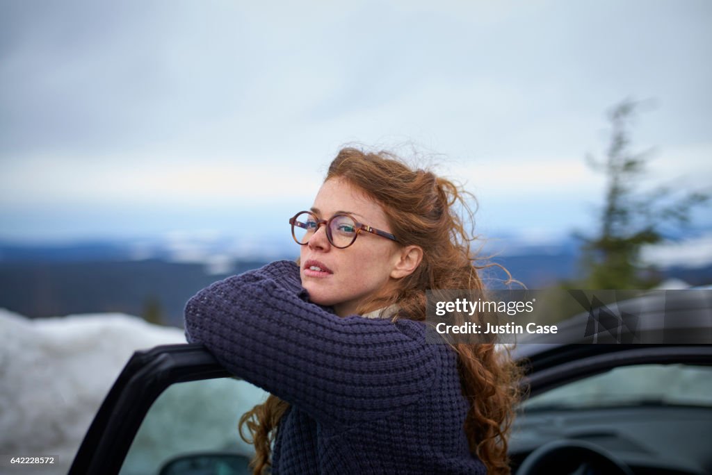 Woman leaning on her car door overlooking landscape while having a break from driving