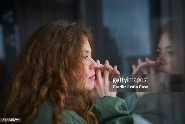 woman looking out of window into her reflection - contemplation stock-fotos und bilder