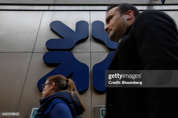 Commuters pass a logo sitting on a wall outside a Royal Bank of Scotland Group Plc bank branch in London, U.K., on Wednesday, Feb. 15, 2017. RBS is...