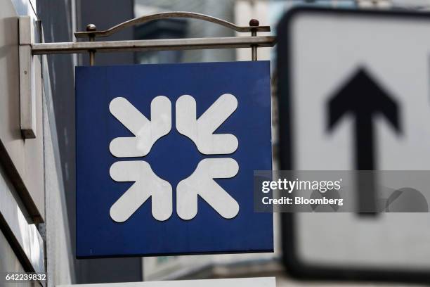 Logo sits on a sign, next to road-direction arrow, outside a Royal Bank of Scotland Group Plc bank branch in London, U.K., on Wednesday, Feb. 15,...