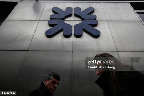 Commuters pass a logo sitting on a wall outside a Royal Bank of Scotland Group Plc bank branch in London, U.K., on Wednesday, Feb. 15, 2017. RBS is...