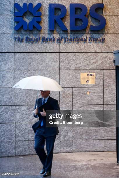 An employee carries an umbrella while leaving the Royal Bank of Scotland Group Plc offices in London, U.K., on Wednesday, Feb. 15, 2017. RBS is...
