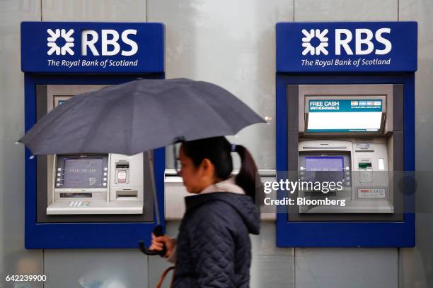 Pedestrian carries an umbrella while passing automated teller machines outside a Royal Bank of Scotland Group Plc bank branch in London, U.K., on...