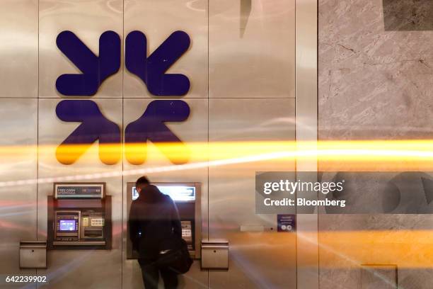 Traffic leaves light trails as a customer uses an automated teller machine outside a Royal Bank of Scotland Group Plc bank branch in London, U.K., on...